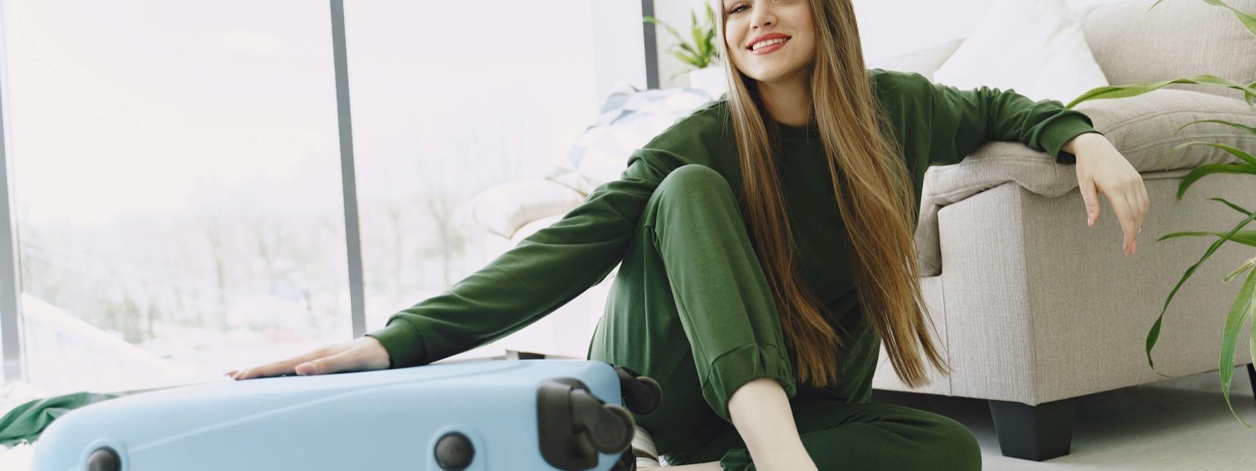 Smiling travel therapist sitting beside a suitcase at home